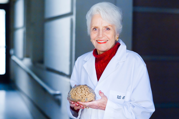 Foto de Maria Diamond, una científica de edad mayor con una bata blanca y un cerebro en sus manos para explicar sus descubrimientos sobre la neuroplasticidad