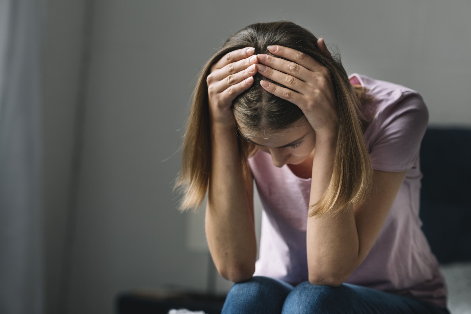 MUJER BLANCA DE CABELLO CASTAÑO SENTADA EN UNA SILLA COLOR NEGRO CON SUS MANOS EN LA CABEZA MIENTRAS PADECE UN ATAQUE DE ANSIEDAD Y BUSCA LA FORMA DE CALMARSE