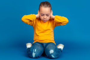 Foto de niño en playera mangalarga naranja,en medio de una habitación vacía con el fondo azul mientras tiene una crisis del trastorno autista