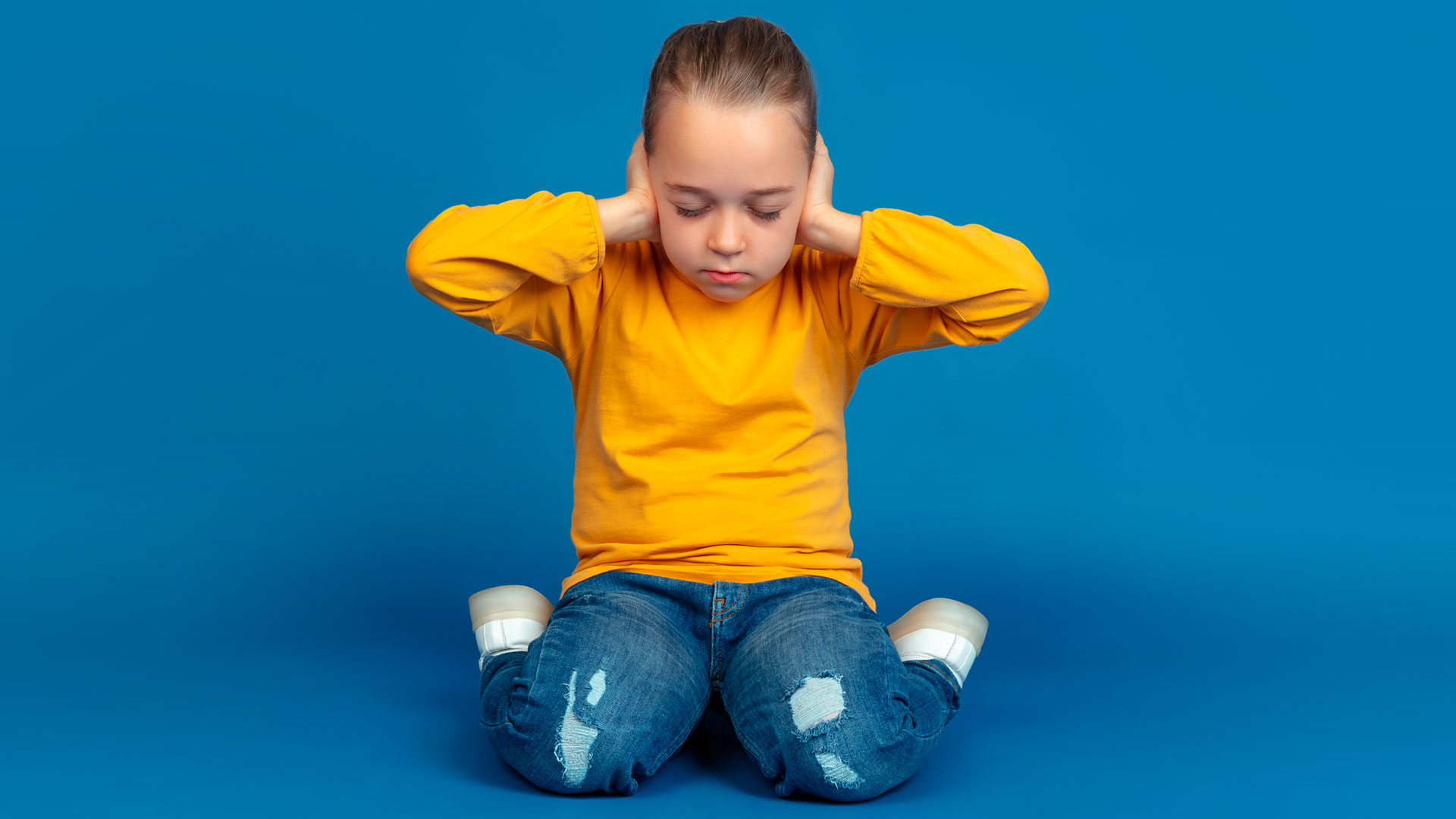 Foto de niño en playera mangalarga naranja,en medio de una habitación vacía con el fondo azul mientras tiene una crisis del trastorno autista